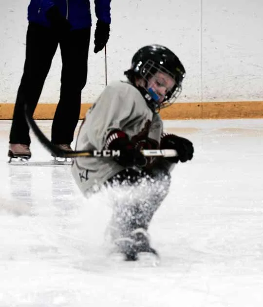 A young hockey player practicing a stop with a spray of ice