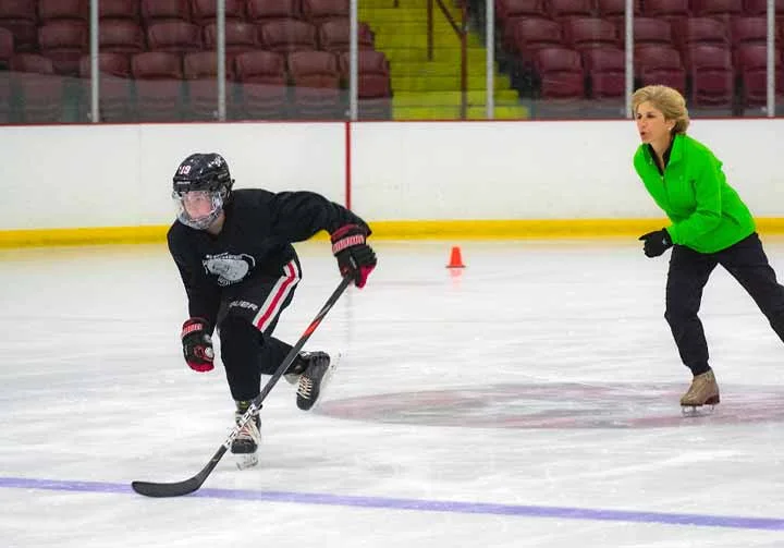Suzy skating alongside a player practicing with a hockey stick