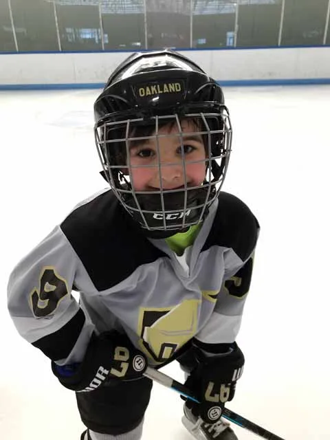 A young skater smiling through a hockey helmet